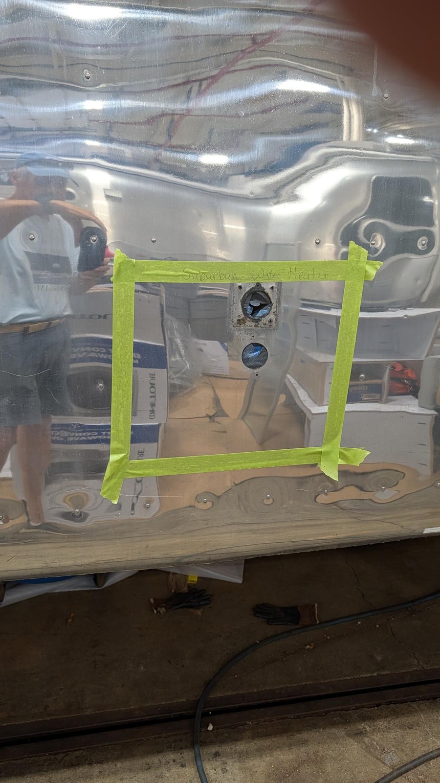 A section of the Airstream's polished shell marked off with green tape and labeled by hand for the placement of a Suburban water heater.